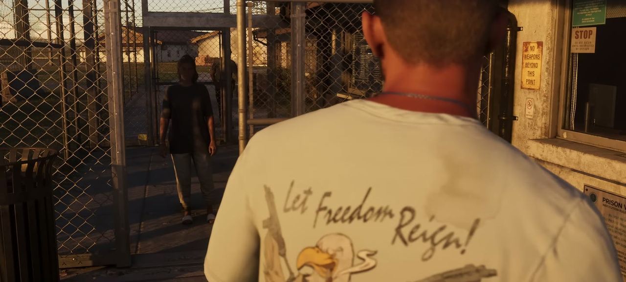 The back of a shirt reading Let Freedom Reign, walking out through a prison gate. Four signs are legible on the gatehouse wall, including a visiting-hours notice issued by order of the state governor.