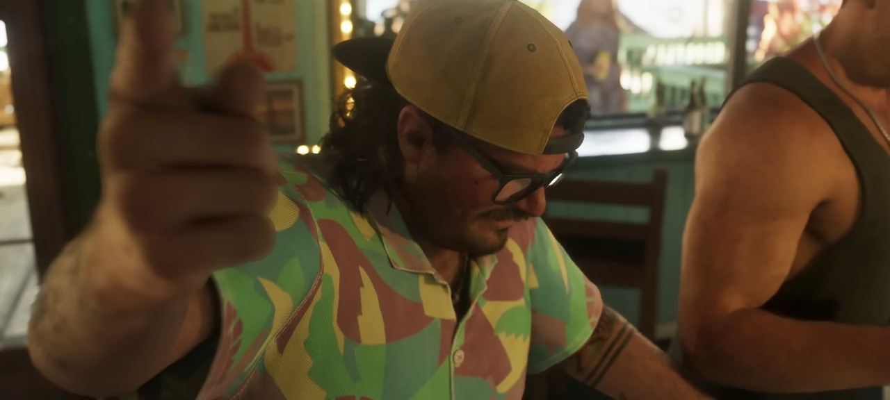 A man in a bucket hat raising a thumb, sunglasses on.